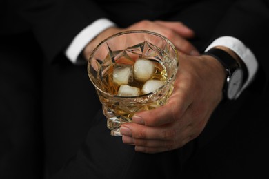 Photo of Man holding glass of whiskey with ice cubes on black background, closeup