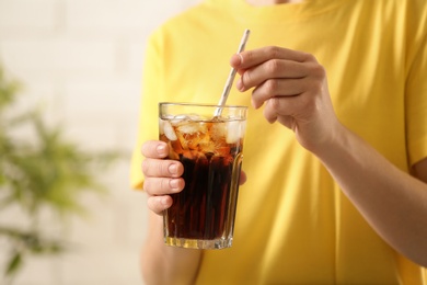 Photo of Woman holding glass of cola with ice on blurred background, closeup. Space for text