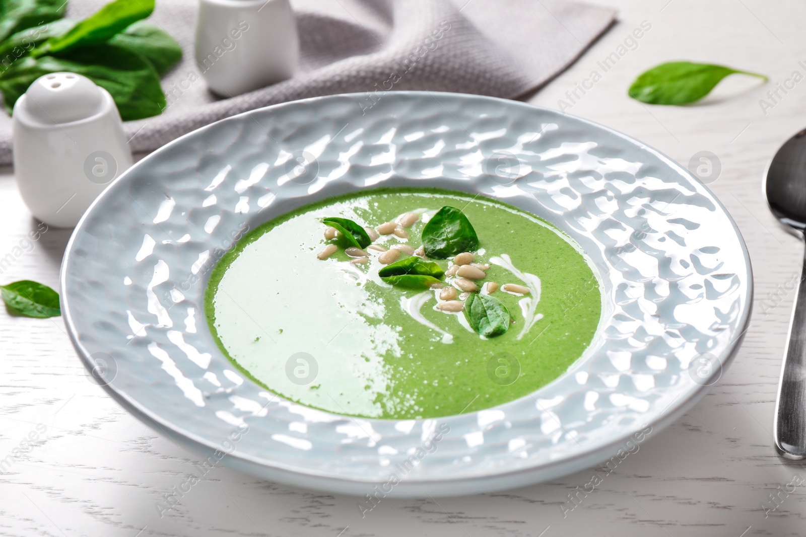 Photo of Plate of healthy green soup with fresh spinach on white wooden table