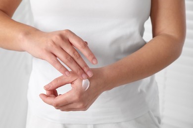 Photo of Woman applying cosmetic cream onto hand on blurred background, closeup