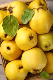 Tasty ripe quince fruits in crate on wooden table, top view