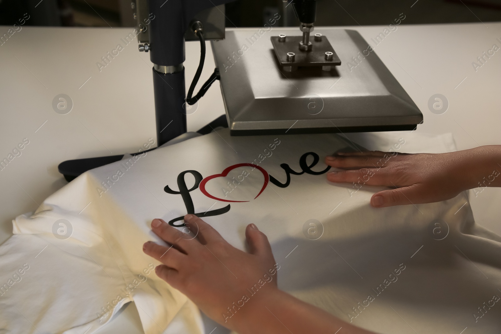 Photo of Printing logo. Woman with t-shirt using heat press at white table, closeup