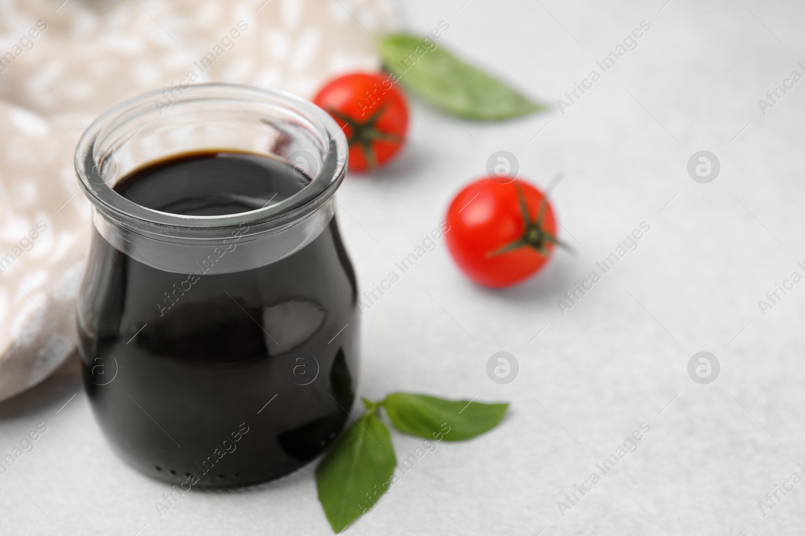 Photo of Glass jar with balsamic vinegar, basil and tomatoes on white table, closeup. Space for text