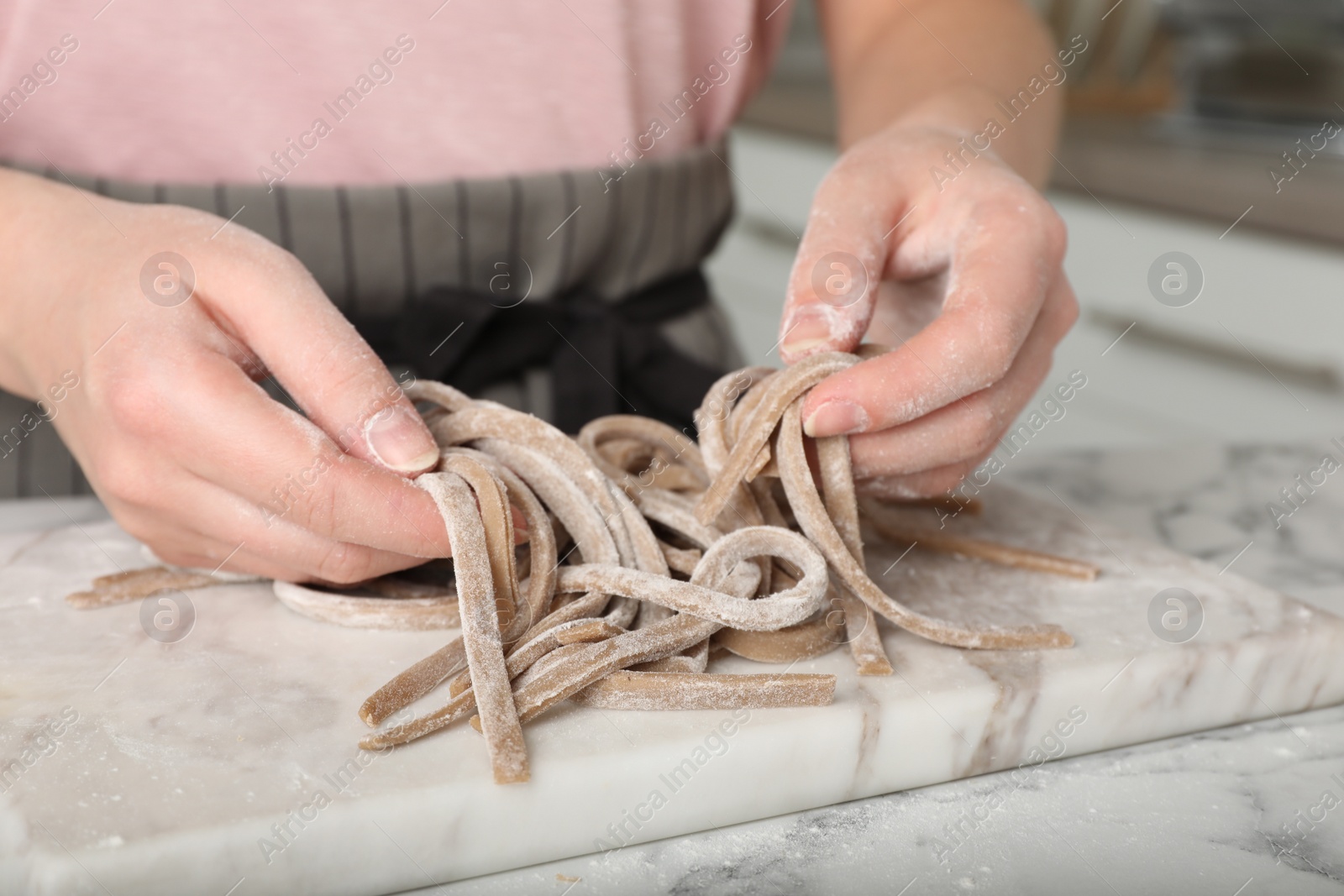 Photo of Woman making soba (buckwheat noodles) at white marble table in kitchen, closeup