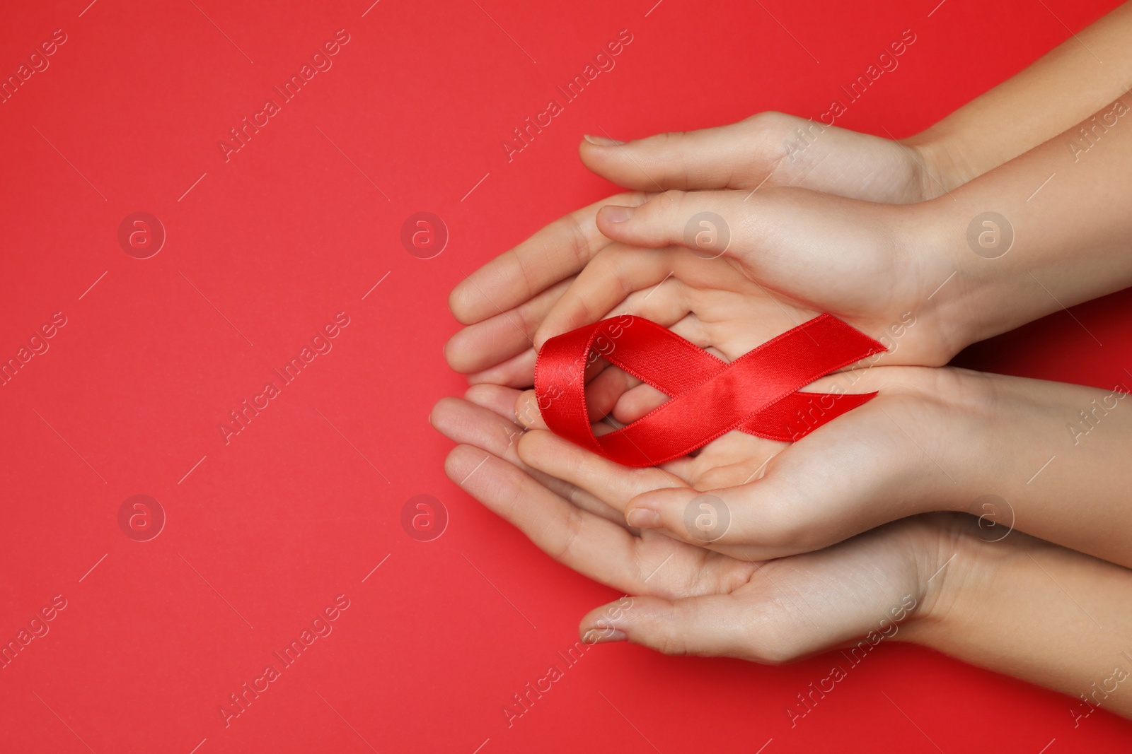 Photo of Woman and girl holding red ribbon on bright background, top view with space for text. AIDS disease awareness