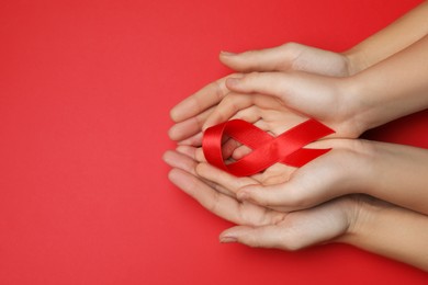 Photo of Woman and girl holding red ribbon on bright background, top view with space for text. AIDS disease awareness