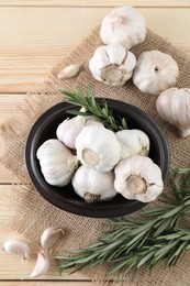 Fresh raw garlic and rosemary on wooden table, flat lay