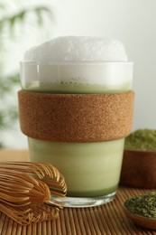 Photo of Glass cup of fresh matcha latte, powder and bamboo whisk on table, closeup