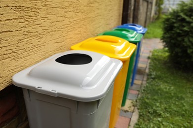 Many colorful recycling bins near yellow wall outdoors