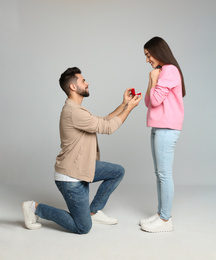 Man with engagement ring making marriage proposal to girlfriend on light grey background