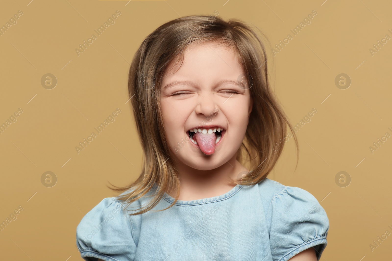 Photo of Emotional little girl showing her tongue on beige background