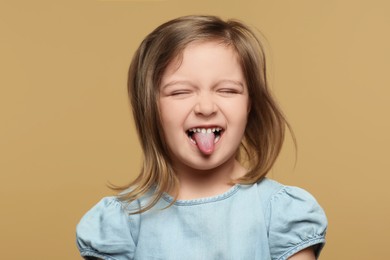Emotional little girl showing her tongue on beige background