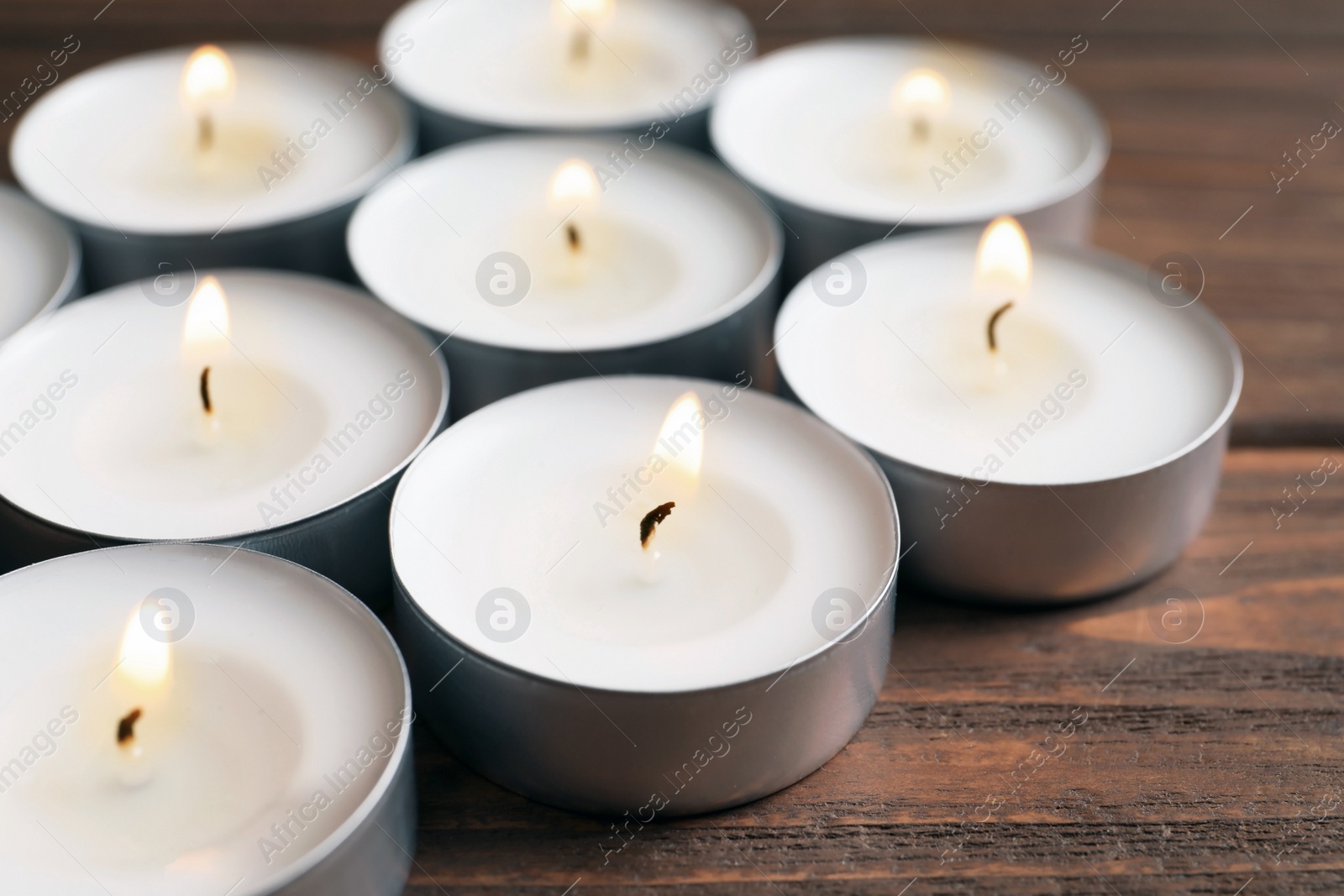 Photo of Small wax candles burning on wooden table, closeup
