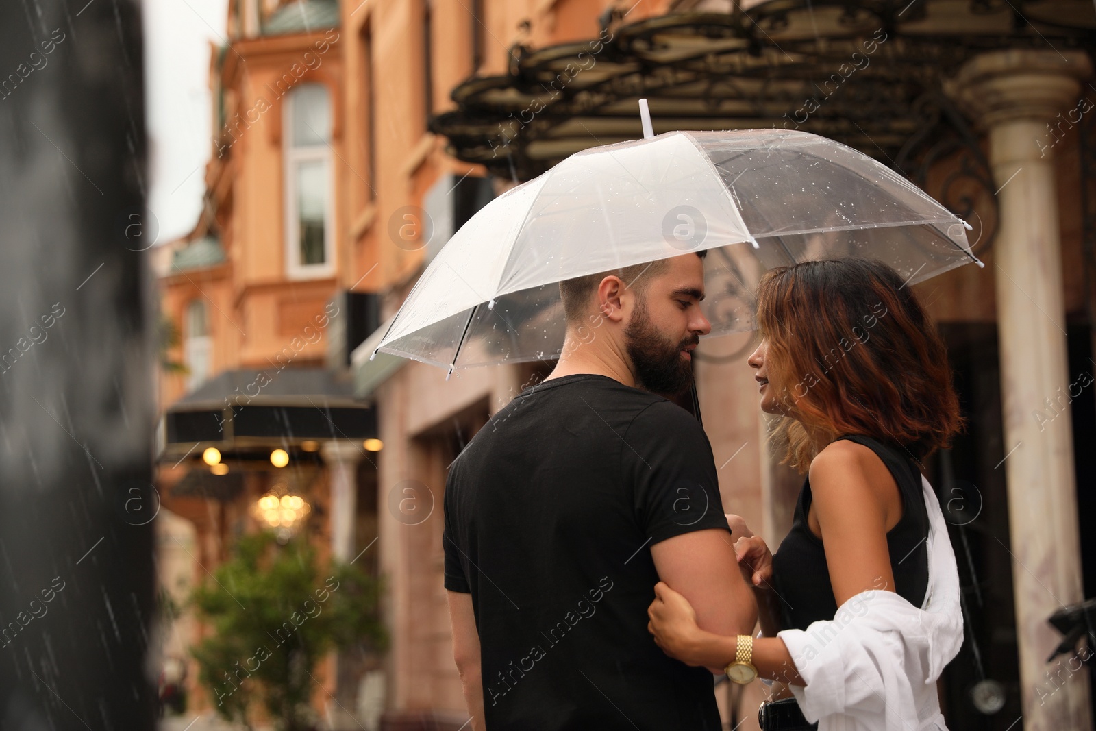 Photo of Young couple with umbrella enjoying time together under rain on city street