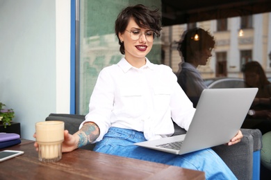 Photo of Young woman working with laptop at desk in cafe