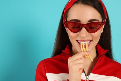 Beautiful young woman eating French fries on light blue background. Space for text