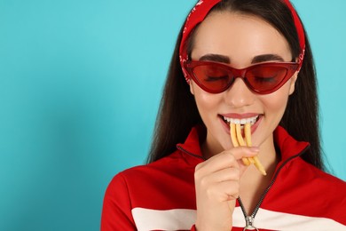 Photo of Beautiful young woman eating French fries on light blue background. Space for text