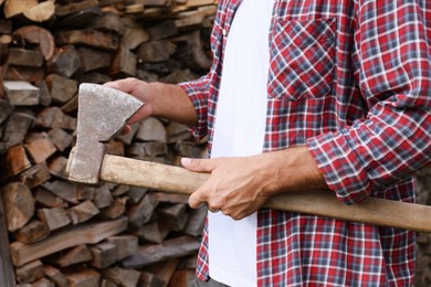 Photo of Man with sharp ax near wood pile outdoors, closeup