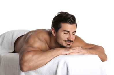 Handsome young man relaxing on massage table against white background. Spa salon