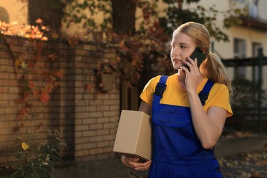 Photo of Courier with parcel talking on smartphone outdoors, space for text. Order delivery