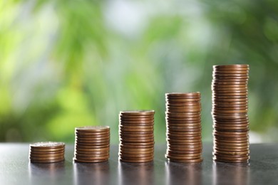 Stacked coins on grey table against blurred green background