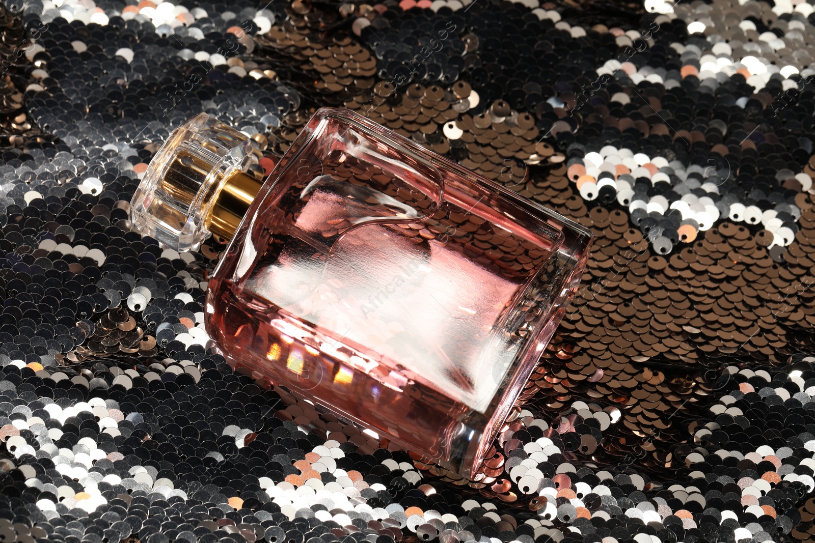 Photo of Luxury perfume in bottle on fabric with silver sequins, above view