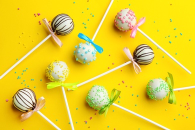 Different tasty cake pops with sprinkles on yellow background, flat lay