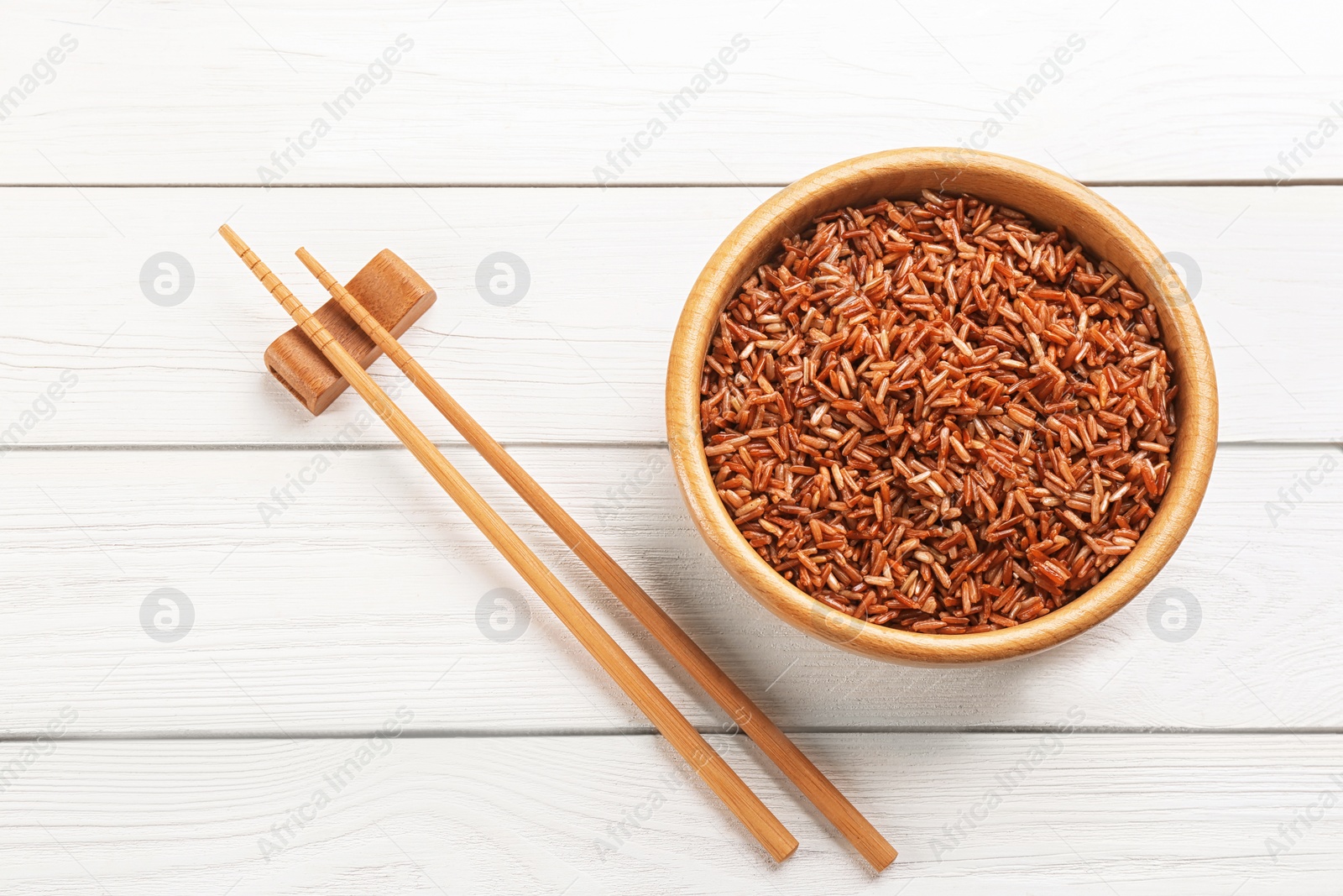 Photo of Tasty brown rice and chopsticks on white wooden table, flat lay