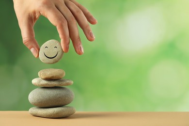 Photo of Woman putting stone with drawn happy face onto stack against blurred background, closeup and space for text. Zen concept