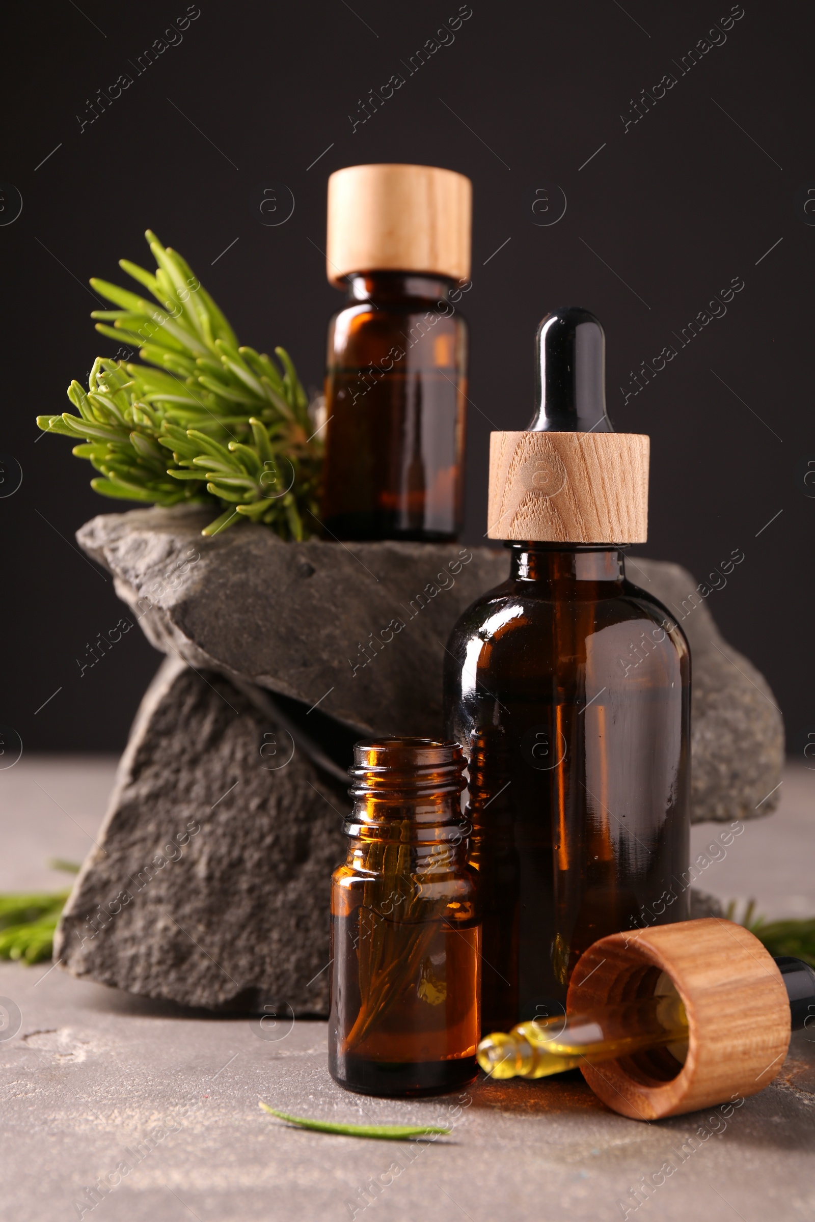 Photo of Essential oil in bottles, dropper and rosemary on grey table