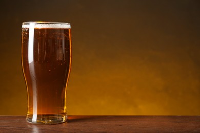 Photo of Glass with fresh beer on wooden table against dark background. Space for text