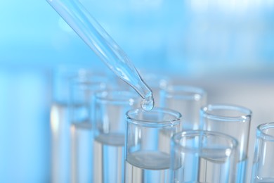 Dripping liquid from pipette into test tube on light background, closeup