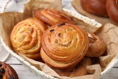 Photo of Delicious rolls with raisins in basket on white table, closeup. Sweet buns