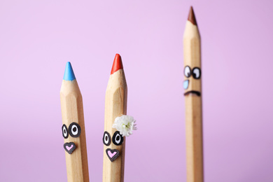 Photo of Pencils with drawn faces on violet background, closeup. Concept of jealousy