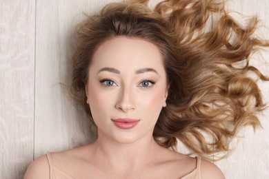 Portrait of beautiful woman with curly hair on wooden floor, top view