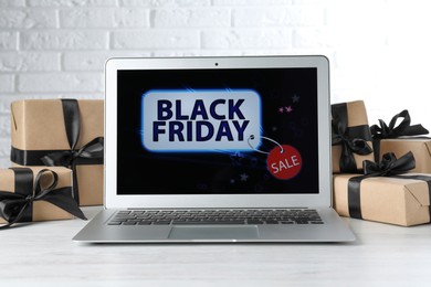Photo of Laptop and gift boxes on white wooden table. Black Friday sale
