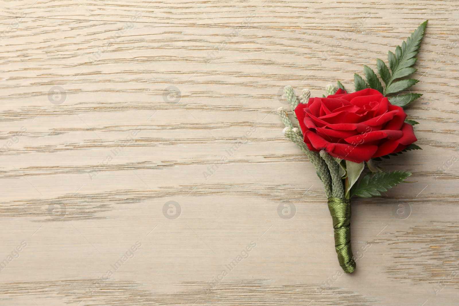 Photo of One stylish red boutonniere on light wooden table, top view. Space for text