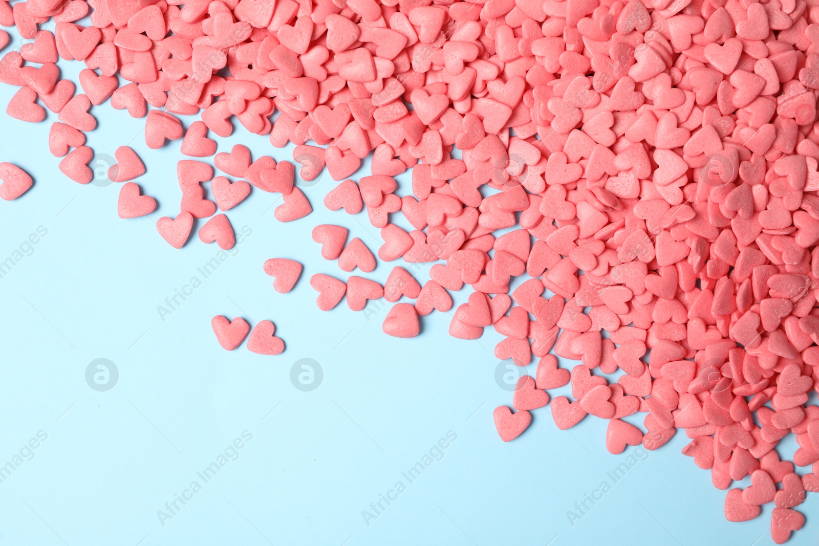 Photo of Bright heart shaped sprinkles on light blue background, flat lay. Space for text