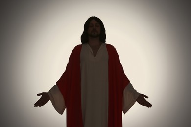 Silhouette of Jesus Christ with outstretched arms on color background