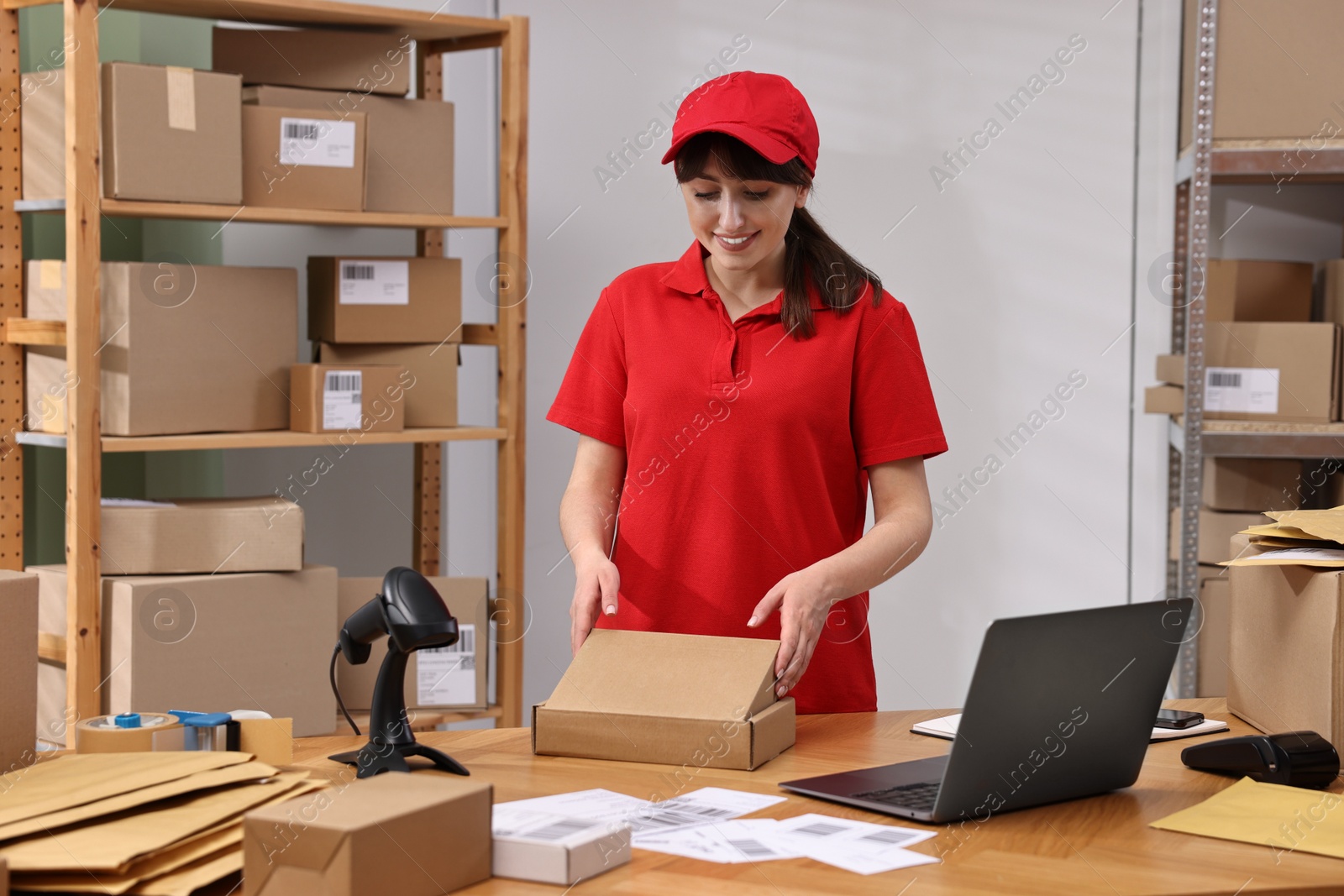 Photo of Post office worker packing parcel at wooden table indoors