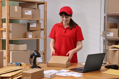 Post office worker packing parcel at wooden table indoors