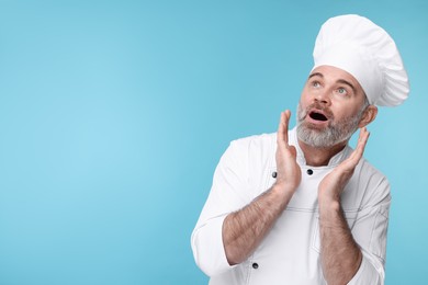 Surprised chef in uniform on light blue background, space for text