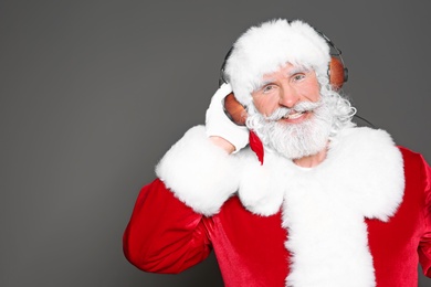 Santa Claus listening to Christmas music on color background