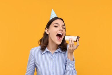 Photo of Happy young woman in party hat eating cheesecake on yellow background