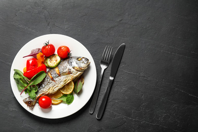 Photo of Delicious roasted fish with lemon and vegetables on dark grey table, flat lay. Space for text