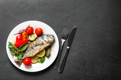 Delicious roasted fish with lemon and vegetables on dark grey table, flat lay. Space for text