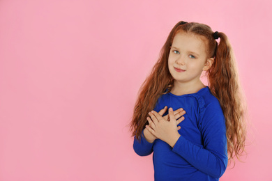 Photo of Cute grateful little girl with hands on chest against pink background. Space for text