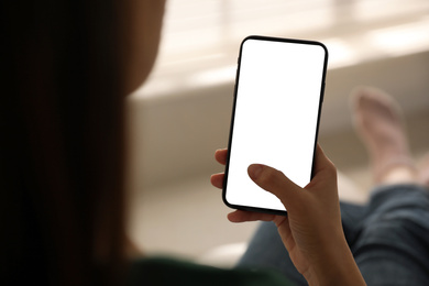 Woman holding mobile phone with empty screen indoors, closeup