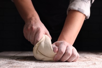 Man kneading dough at wooden table on dark background, closeup