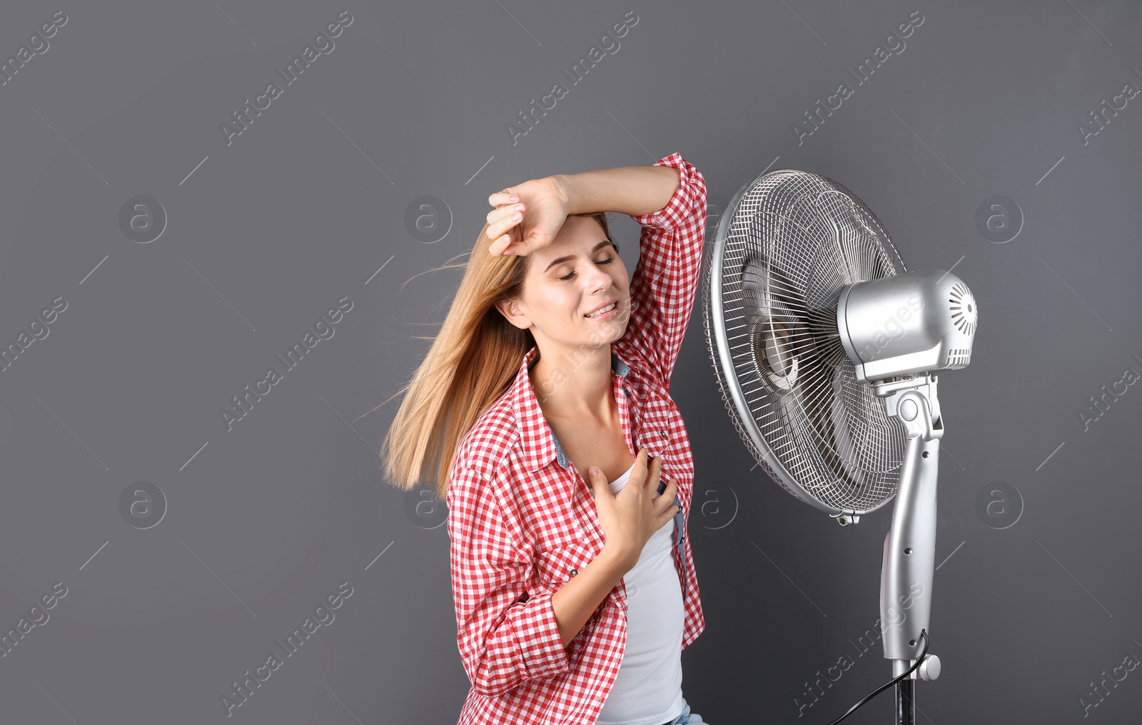 Photo of Woman refreshing from heat in front of fan on grey background